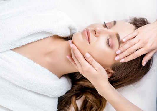 Masaje facial manual en la frente y la mandíbula de una mujer recostada con albornoz blanco.